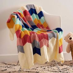 a teddy bear sitting next to a colorful blanket on a white chair in a room