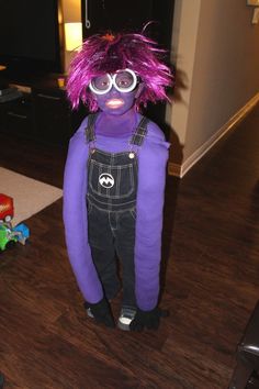 a purple monster with pink hair and glasses standing in front of a television set on a wooden floor