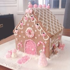 a gingerbread house decorated with pink icing and sprinkles on a white plate