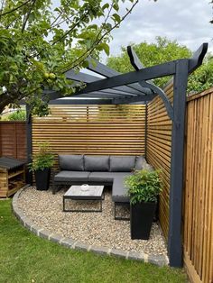 an outdoor seating area in the middle of a garden with wooden fence and planters