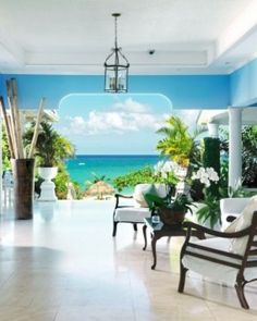 a living room with blue walls and white furniture on the floor, overlooking the ocean