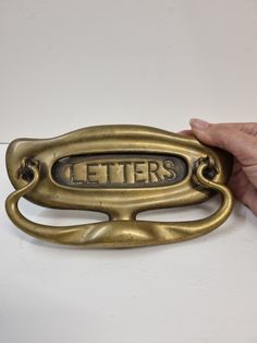 a hand holding an old brass door handle that says letters