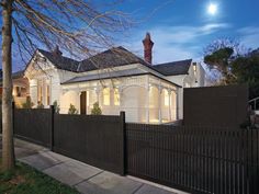 a white house with a black fence and trees in front of it at night time