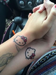 two people holding hands with hello kitty tattoos on their arm and wrist, in front of a car