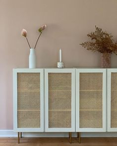 a white cabinet with three doors and two vases on the top, against a pink wall