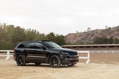 a black jeep is parked in front of a white fence and some hills with trees