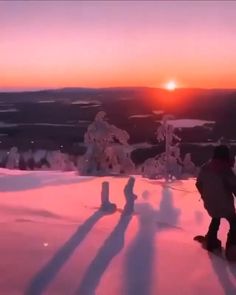 a man riding a snowboard down a snow covered slope at sunset with the sun behind him