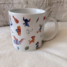 a white coffee cup with winnie the pooh characters on it sitting on a bed