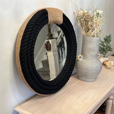 a round mirror sitting on top of a wooden table next to a vase with flowers