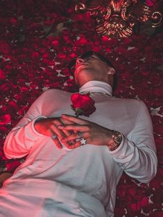 a man laying on the ground surrounded by red rose petals with his eyes closed and hands clasped