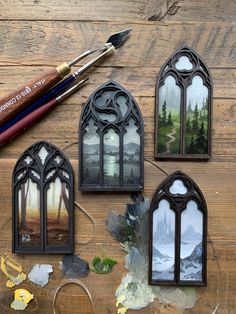 three stained glass windows sitting on top of a wooden table next to paintbrushes