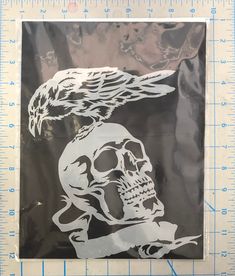 a sticker with a skull and a bird on it's head in front of a ruler