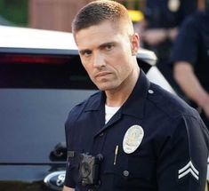 a police officer standing in front of a car with his hand on his hip and looking at the camera