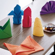 folded napkins and plates on a table with paper origami boats in the background