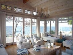 a living room filled with white furniture and lots of windows overlooking the water in front of them