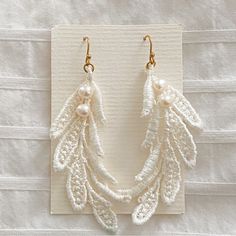 two pairs of white beaded earrings with pearls hanging from hooks on a piece of cloth