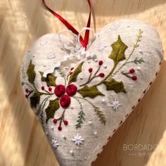 a white heart shaped ornament with holly and berries