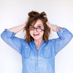 a woman with glasses is holding her hair in front of her head and smiling at the camera