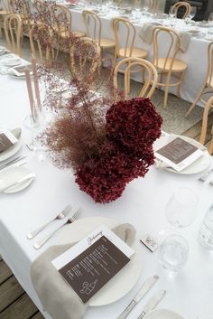 the table is set with white linens and place settings, silverware and flowers