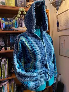 a crocheted hooded jacket is displayed in front of a bookshelf