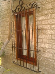 a window with iron bars on the side of a stone building next to a tree