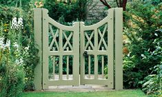 an open gate in the middle of a garden with green grass and flowers around it