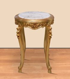 an ornately decorated gold table with marble top on wooden floor in front of beige wall