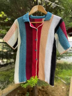 a colorful crocheted shirt hanging on a clothes line with trees in the background