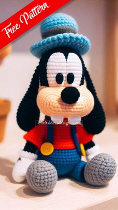 a crocheted mickey mouse is sitting on the floor wearing a blue hat and red shirt