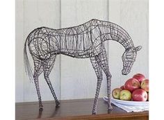 a wire horse and bowl of apples on a table in front of a white wall