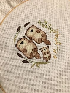 two brown and white cows sitting on top of each other in front of a cross stitch pattern