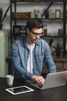 a man sitting at a table with a laptop computer in front of him and looking at the screen