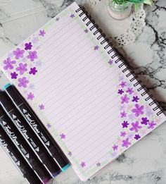 three pens sitting on top of a notepad next to two empty notebooks and a potted plant