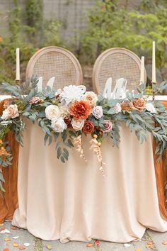 an arrangement of flowers and greenery decorates the head table at this outdoor wedding reception