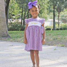 Show your team spirit by wearing this Purple Gingham Avery Dress. Features flutter sleeves and side-tie bows in a purple gingham. Back buttons for closure. Personalized the look by adding a monogram! LSU tigers kids smocked gameday outfit | kids smocked outfit | gameday essentials | kids closet inspiration | kids trends | outfit trends | kids fashion | kids fall clothing | football | football game | geaux | tigers | lau game | lsu gameday outfit Kids Tailgate, College Football Outfits, Kids Smock, Kids Fall Outfits, Tiger Kids, Purple Gingham, Monogram Outfit, Tailgate Outfit