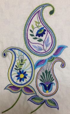 an embroidered piece with flowers and paisleys on the side, sitting on top of a white table cloth