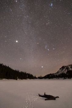 a person is laying in the snow with their feet up and looking at the stars above them