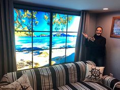 a man standing next to a couch in front of a large window with a painting on it