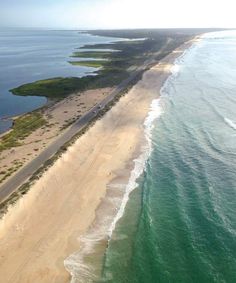 an aerial view of the beach and ocean with cars driving on it's side