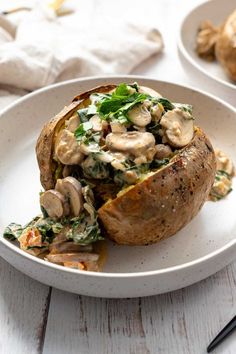 a baked potato with mushrooms and spinach on it in a white bowl next to a fork