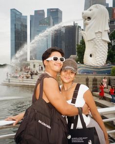 two people standing next to each other in front of a fountain