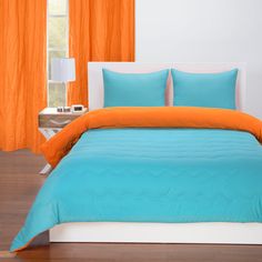 an orange and blue bed in a white bedroom with wood flooring next to a window