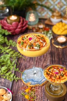 two glasses filled with food sitting on top of a table next to plates and candles