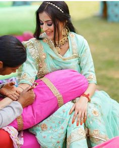 a woman in a green and pink dress is giving something to a child on her lap