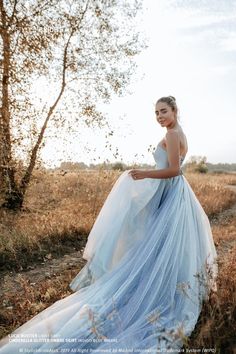 a woman in a blue and white dress standing on a dirt road near a tree