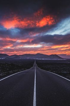 an empty road in the middle of nowhere with mountains in the background at sunset or dawn