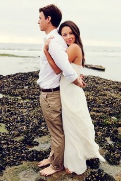 a man and woman standing next to each other on rocks near the ocean with their arms around each other