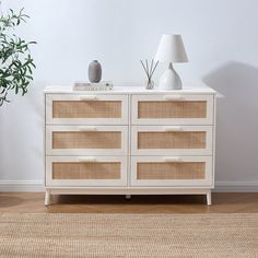 a white dresser with wicker drawers and a lamp next to it on a wooden floor