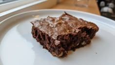 a piece of chocolate cake sitting on top of a white plate next to a window