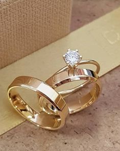 two gold wedding rings sitting on top of each other with a diamond in the middle